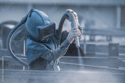 Sand blasting process, Industial worker using sand blasting process preparation cleaning surface on steel before painting in factory workshop. photo