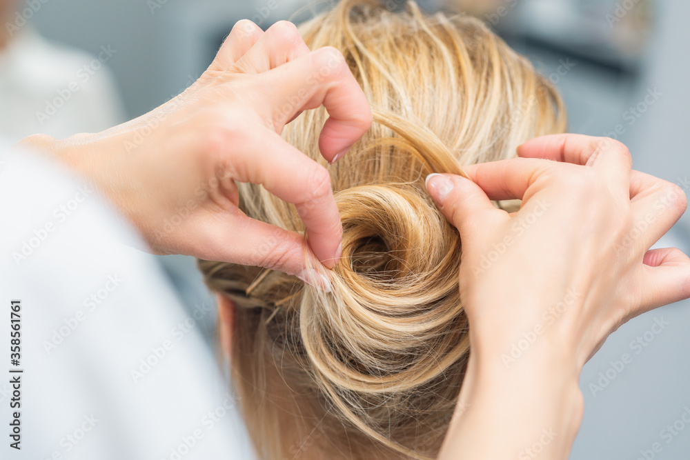 Obraz premium Close up rear view of hairdresser making hairstyle for long hair of blonde woman.