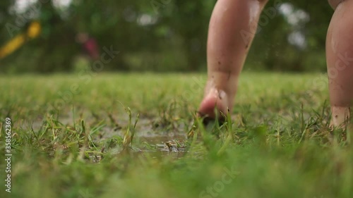 Clouse up portrait of toddlers bare feet, a child jumping in the grass through a puddle, a happy childhood, have fun. A kid having loads of fun jumping in mud puddle