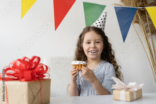 Cute Caucasian Girl Celebrates Birthday. Eating a delicious cake at the festive table. Gifts for the birthday.