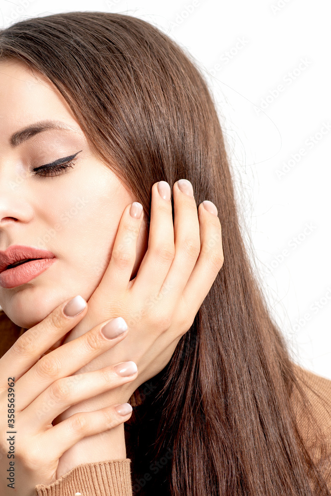 Close up portrait of pretty young woman touching her face by her hand with beige manicure on white background. Close up portrait of pretty young woman touching her face by her hand with beige manicure on white background.