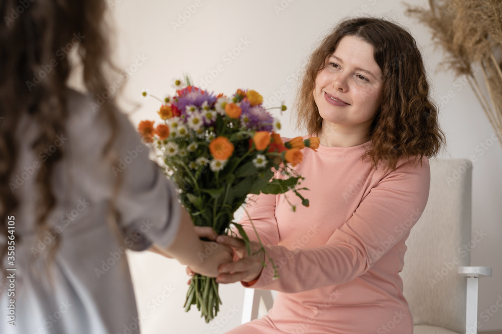 Mothers Day. Mother and daughter. A girl gives a woman a bouquet of beautiful colored wildflowers. The young lady has wavy dark long hair and her mother has a haircut and she is happy. Mothers Day. Mother and daughter. A girl gives a woman a bouquet of beautiful colored wildflowers. The young lady has wavy dark long hair and her mother has a haircut and she is happy.