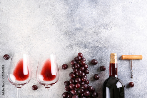 Photos Flat lay composition with two glasses of vintage red wine, bunch of grapes & corkscrew on grunged concrete table background