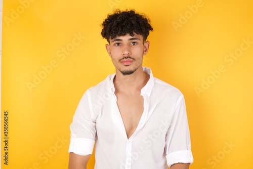Close up studio shot of handsome young mixed race man model with curly dark hair looking at camera with charming cute smile while posing against white blank copy space wall for your content