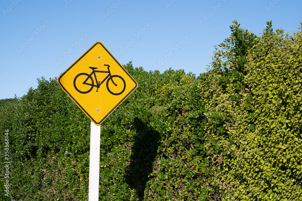Bicycle road sign next to green leaves background with blue sky.
