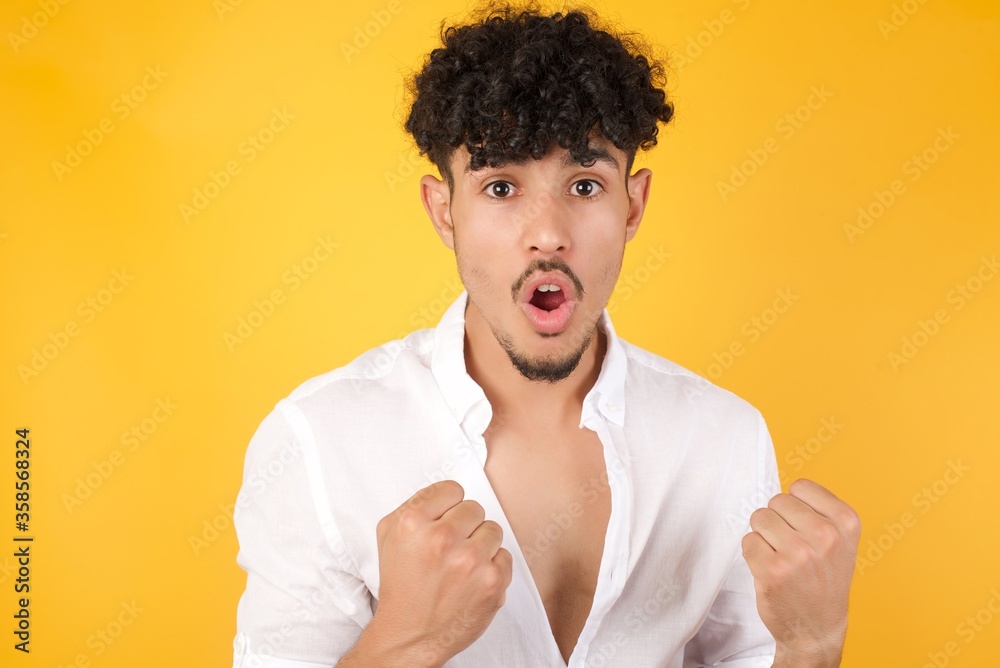 Waist up portrait of strong successful determined young male winner in casual clothes raising arms, clenching fists, exclaiming GOAL with joy and excitement. Victory, success and achievement concept. Waist up portrait of strong successful determined young male winner in casual clothes raising arms, clenching fists, exclaiming GOAL with joy and excitement. Victory, success and achievement concept.