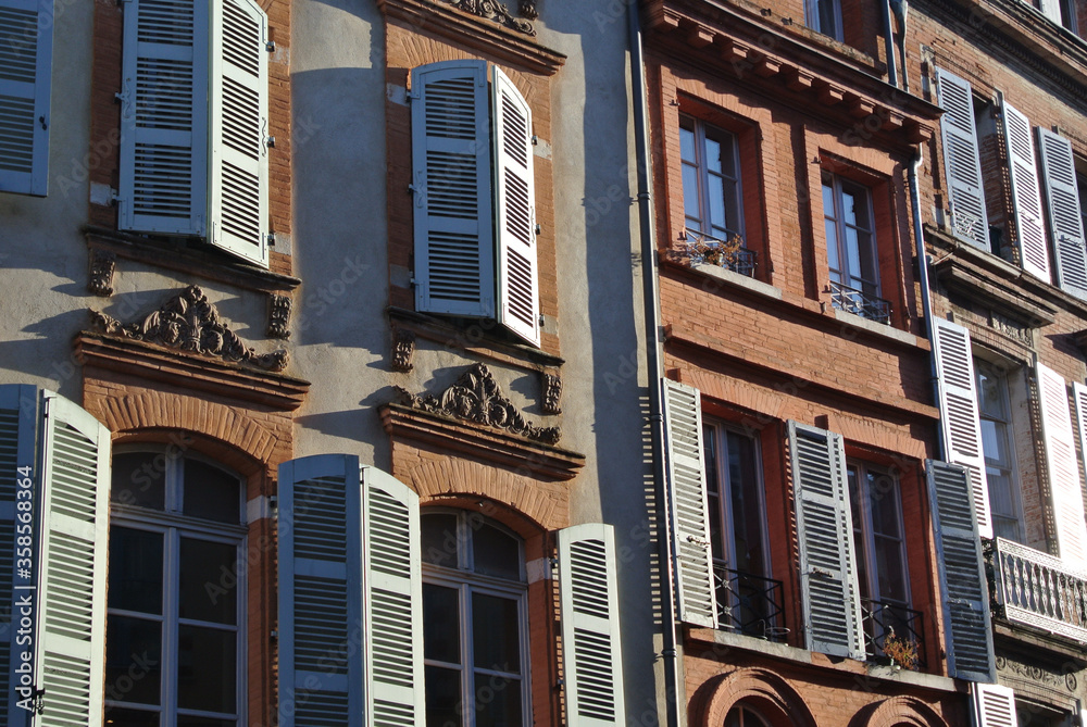 Classical facades of vivid colours with windows and shutters under sun light. Photo from outside. North of France