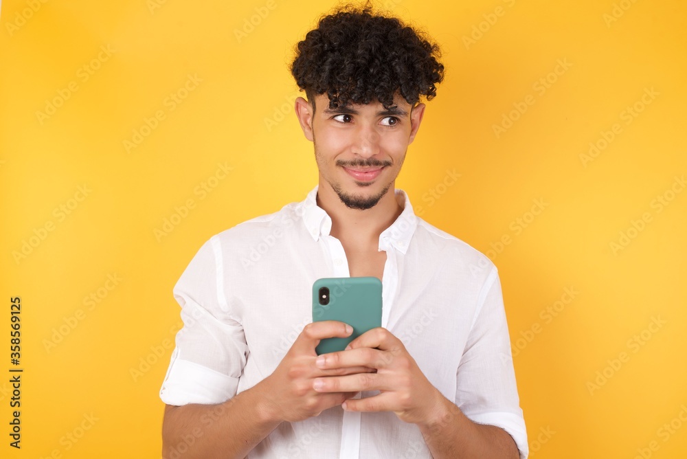 Horizontal shot of pretty young male with afro hair looks with bugged eyes, holds modern smart phone, receives unexpected message from friend, reads reminder, isolated over yellow background. Horizontal shot of pretty young male with afro hair looks with bugged eyes, holds modern smart phone, receives unexpected message from friend, reads reminder, isolated over yellow background.