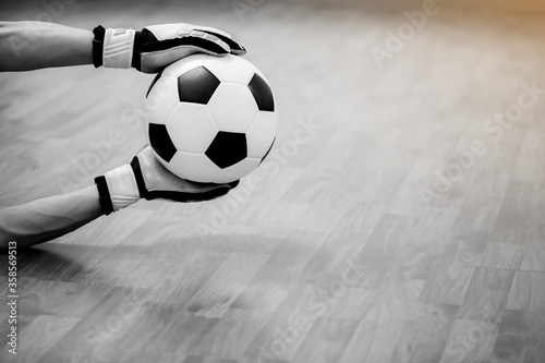 Black and white image of ball in hands of futsal goalkeeper on wooden futsal floor. Indoor soccer sports hall. Football futsal player, ball, Sports background. Youth futsal league. photo