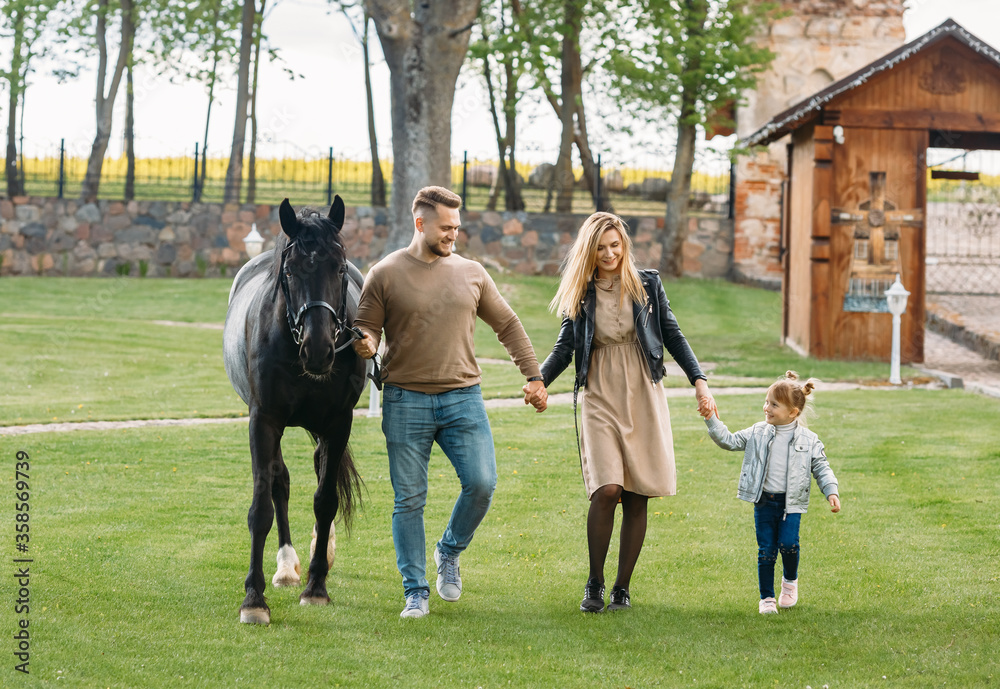 Mother, father and daughter next to a horse. Little girl in the summer field. Family plays with a horse Mother, father and daughter next to a horse. Little girl in the summer field. Family plays with a horse