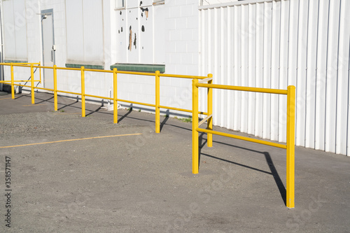 Yellow fences for walkway close to white wall of factory.