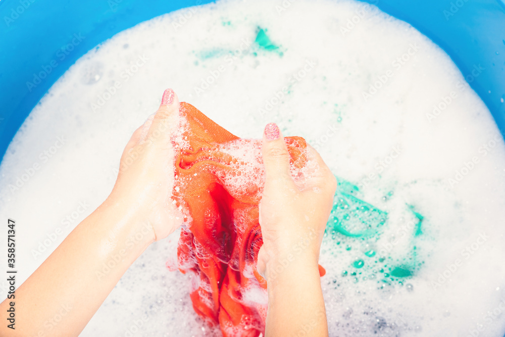 Fototapeta premium Closeup young Asian woman use hands washing color clothes in basin with detergent have soapy bubble water, studio shot background, laundry concept