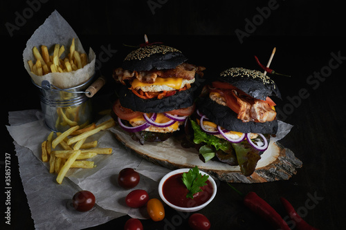 black double burgers on a wooden board and dark background with fries tomatoes