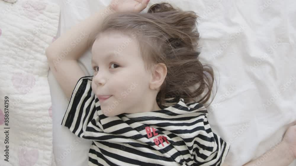 Close-Up Portrait of Little Happy Baby Preschool Girl Lying on a Bed, Top View Close-Up Portrait of Little Happy Baby Preschool Girl Lying on a Bed, Top View