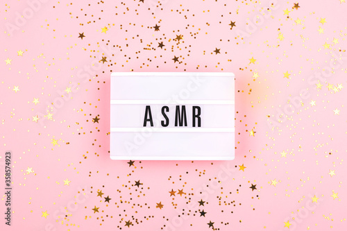 The lamp with letters ASMR on pink background. Decorated with confetti. Sound and visual practice for anxiety, stress and panic relief. Flat-lay.