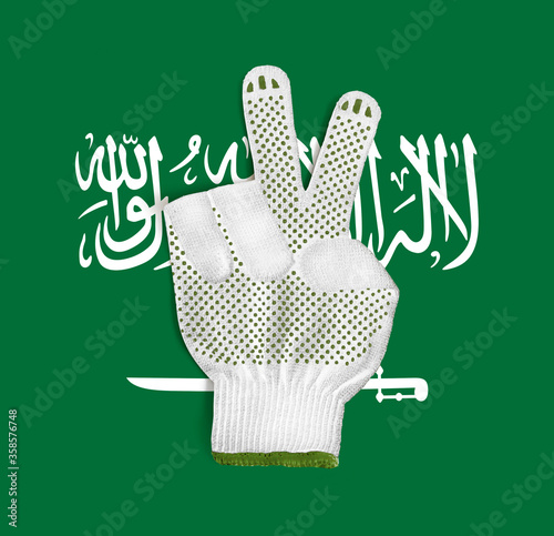 Construction gloves with a gesture of victory on the background of the flag of Saudi Arabia
