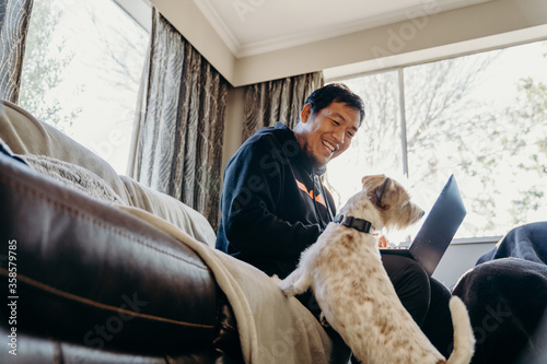 Asian man work from home by laptop with his dog in living room.