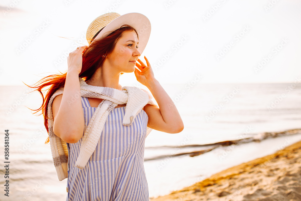 Young beautiful long haired woman with hat smiling at the beach of sea or ocean at sunset. Calm evening, romance. Young beautiful long haired woman with hat smiling at the beach of sea or ocean at sunset. Calm evening, romance.
