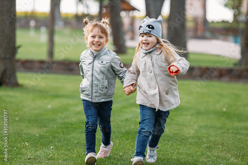 Two happy cute girls running in the park holding hands