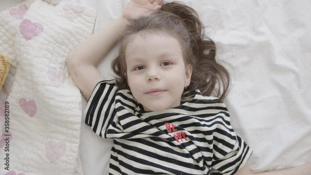Close-Up Portrait of Little Happy Baby Preschool Girl Lying on a Bed, Top View Close-Up Portrait of Little Happy Baby Preschool Girl Lying on a Bed, Top View