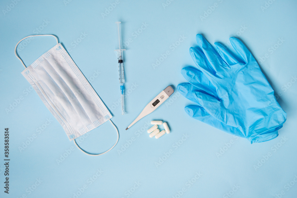 Blue latex gloves on a blue background lie with pills, medical mask, thermometer and syringe. The concept of health and self-control for viruses and epidemics. Close-up Blue latex gloves on a blue background lie with pills, medical mask, thermometer and syringe. The concept of health and self-control for viruses and epidemics. Close-up