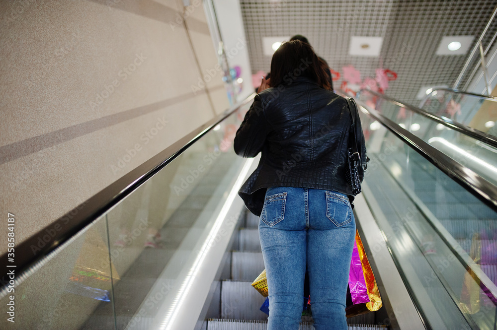 Back of african-american woman walking with coloured shopping bags in mall shopping center on escalator.