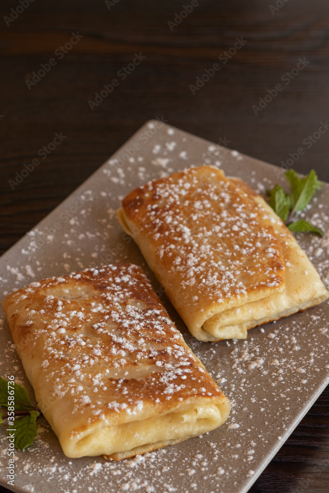 Pancake roll with with powdered sugar or confectioner sugar. Wooden background. Close up Pancake roll with with powdered sugar or confectioner sugar. Wooden background. Close up