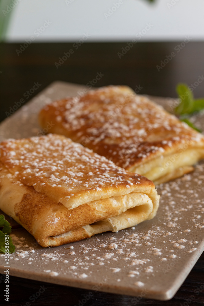 Pancake roll with with powdered sugar or confectioner sugar. Wooden background. Close up