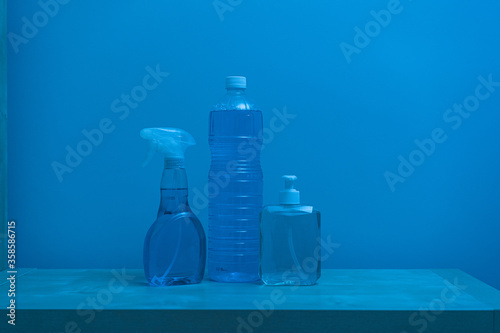 Plastic transparent bottles of different sizes and shapes with colorless liquid inside and white lids locating on shelf against blue wall photo