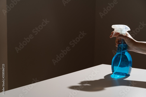 Crop anonymous person pushing dispenser mechanism and directing white cleaner flow on black wall while bottle being placed on white table with shadows photo