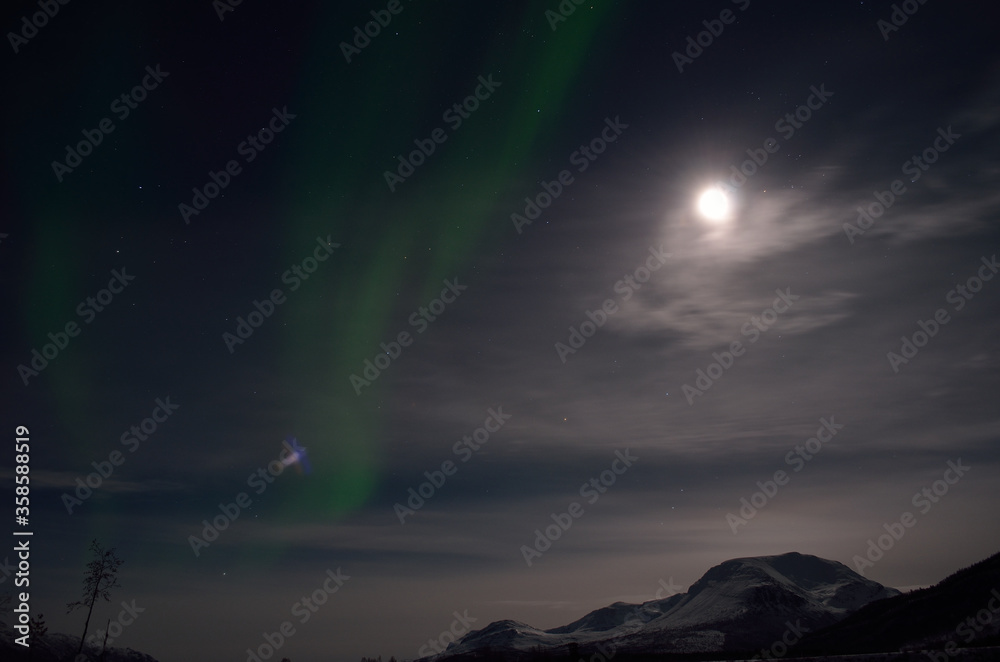 aurora borealis, northern light over snowy winter landscape with mountain and full moon at night