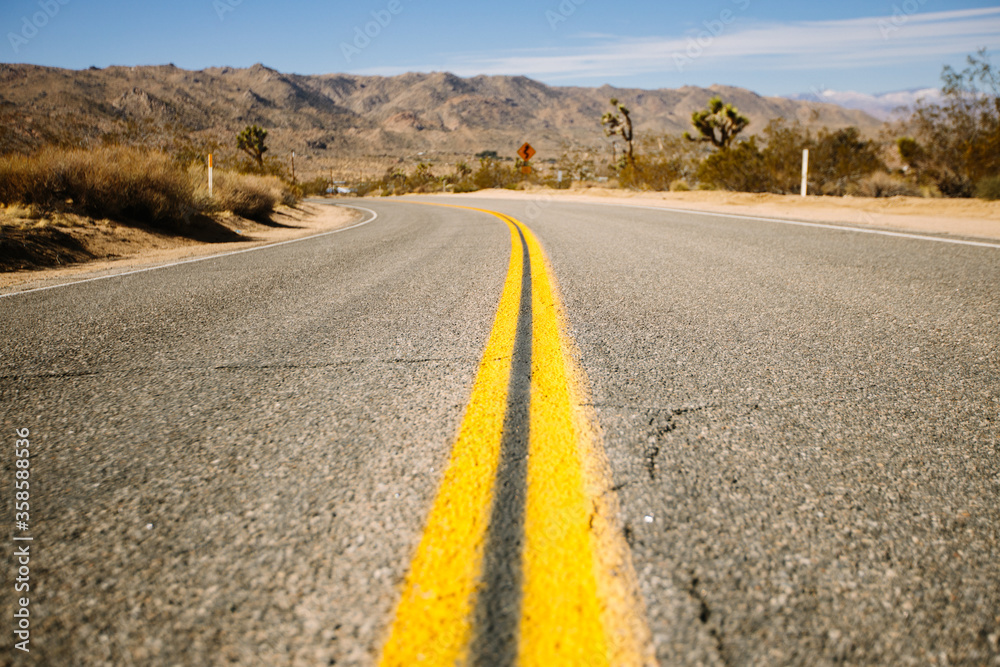 Straight asphalt road going through sandy terrain with dry grass and mountains on background of cloudy sky on heat day in California Straight asphalt road going through sandy terrain with dry grass and mountains on background of cloudy sky on heat day in California