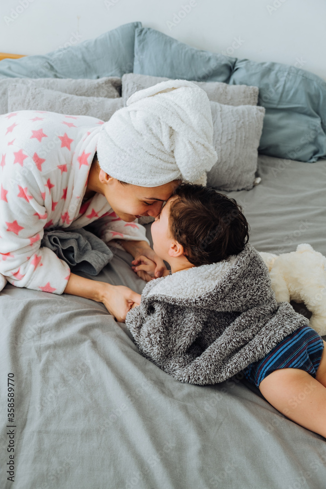 From above of content woman in bathrobe having fun with little boy on soft bed looking at each other From above of content woman in bathrobe having fun with little boy on soft bed looking at each other
