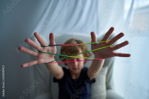 Closeup of hands of boy playing cats cradle game and demonstrating basic figure made with colorful string while spending free time at home