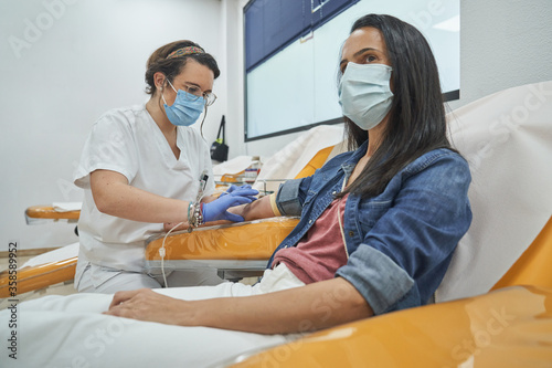 Side view of young woman in protective mask sitting in medical armchair during blood transfusion procedure in contemporary hospital