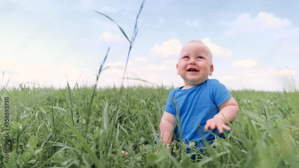 4k. baby sitting crawling on green grass and smiling broadly. Excited cute little caucasian child. Happy childhood and baby healthcare