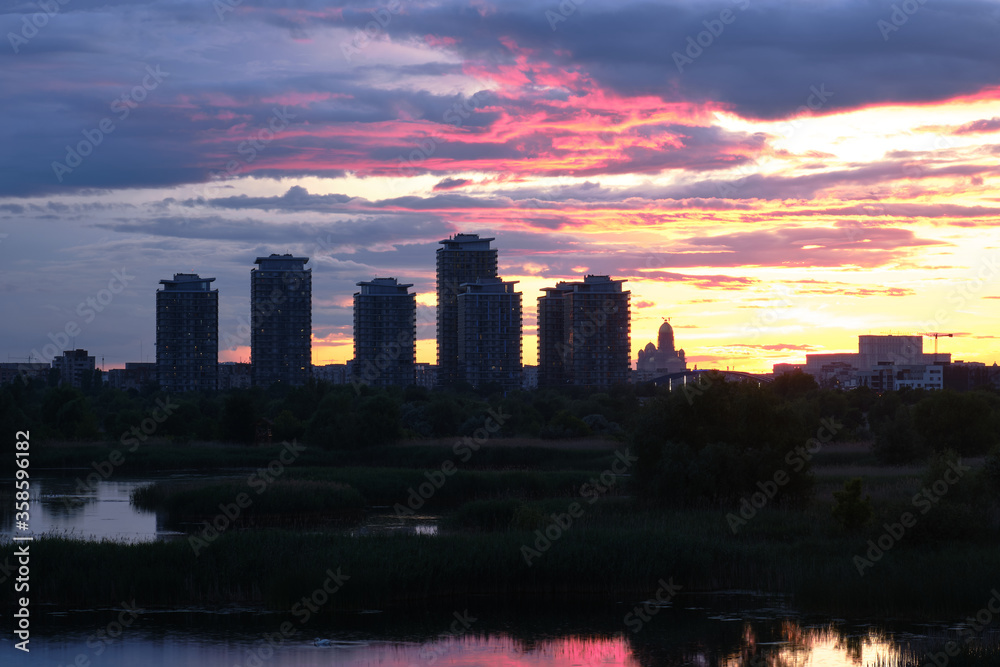 Bucharest city skyline seen from Vacaresti Park Nature Reserve at sunset, with skyscraper towers and landmarks Palace of Parliament and People's Salvation Cathedral to the right.