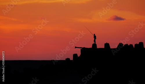 silhouette of man fishing on the shore during sunset