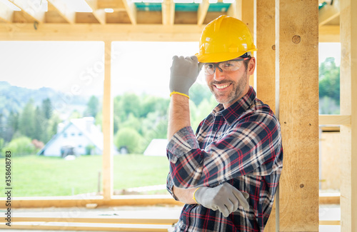 Smiling worker on building site with frame house construction in background