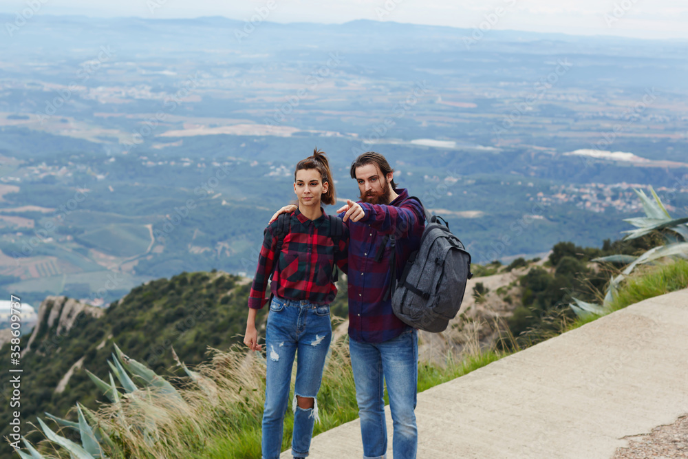 Beautiful young couple admiring the view while out hiking during autumn, backpackers enjoying view standing on mountain trail on high altitude