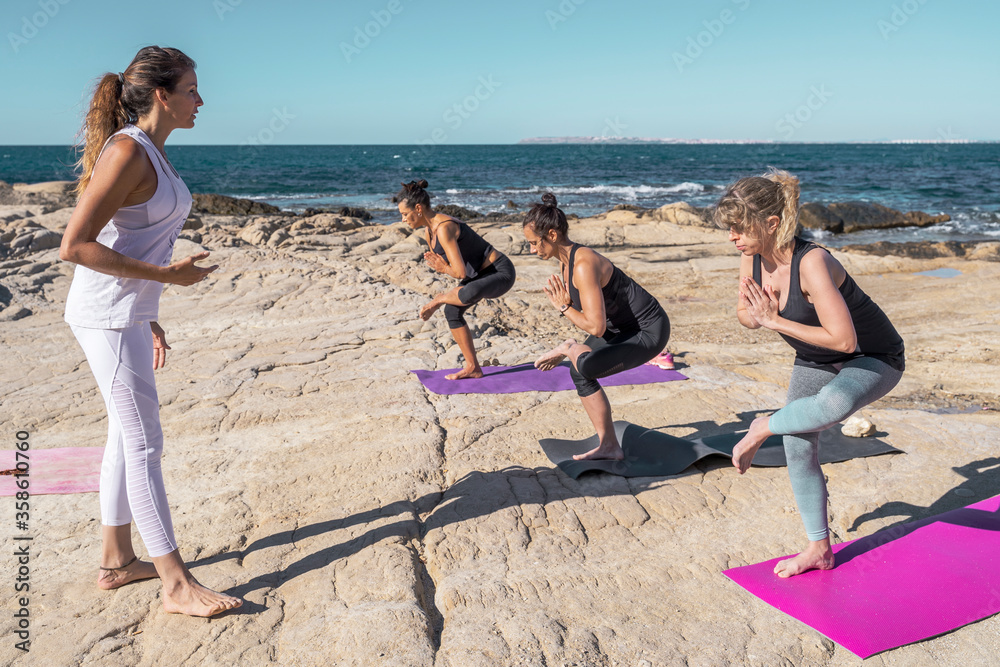 Fototapeta premium Group of people in a yoga class on the beach on sunny day. The group of people is made up of men and women of different ages dressed in sports clothes.