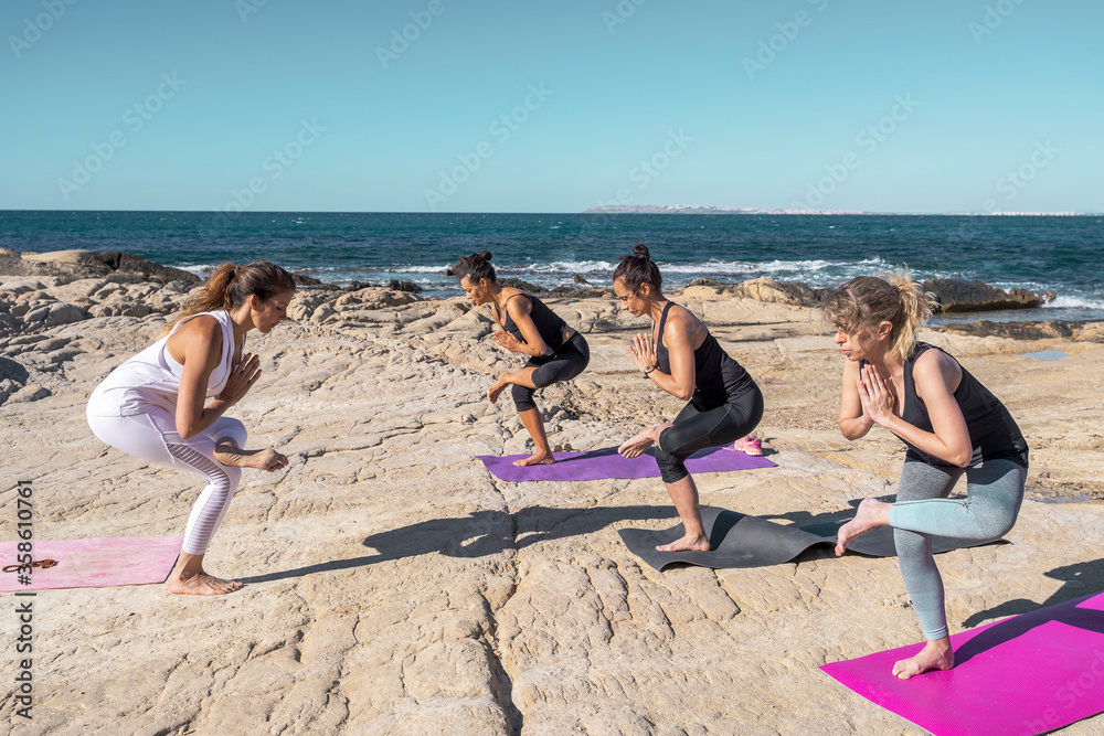 Fototapeta premium Group of people in a yoga class on the beach on sunny day. The group of people is made up of men and women of different ages dressed in sports clothes.