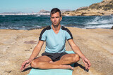 One man meditating on a rocky beach in sunny day in lotus pose