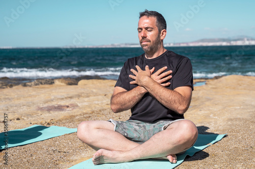 One man meditating on a rocky beach in sunny day in lotus pose.