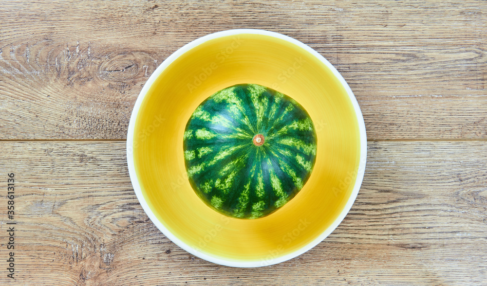small watermelon on a yellow plate on a wooden tabletop small watermelon on a yellow plate on a wooden tabletop