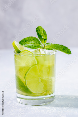 One glass with iced green matcha tea with lime, ice and fresh mint on light grey backdrop closeup. Vertical orientation. Selective focus.