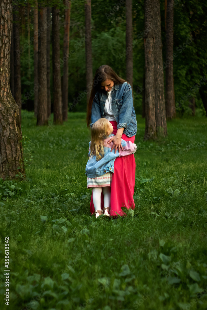 Fototapeta premium happy child girl hugs her mom standing on the grass in the park
