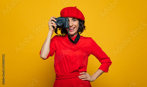 I'm making a photo! Half-length photo of a cute woman on her vacation, french style dressed, carrying a camera on a strap on her neck, with an open mouse, ready to make a photo.