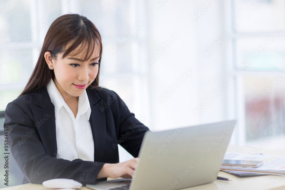 Beautiful Asian businesswomen wearing a black suit is smiling confidently while typing labtop. Asian business women Concept Beautiful Asian businesswomen wearing a black suit is smiling confidently while typing labtop. Asian business women Concept