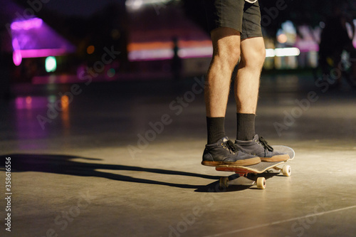 Photography of skateboarder's legs, shoes and skate in night park. Skateboarder getting ready to do the trick to jump. Sportive lifestyles of youth. Dangerous risk speed sports.